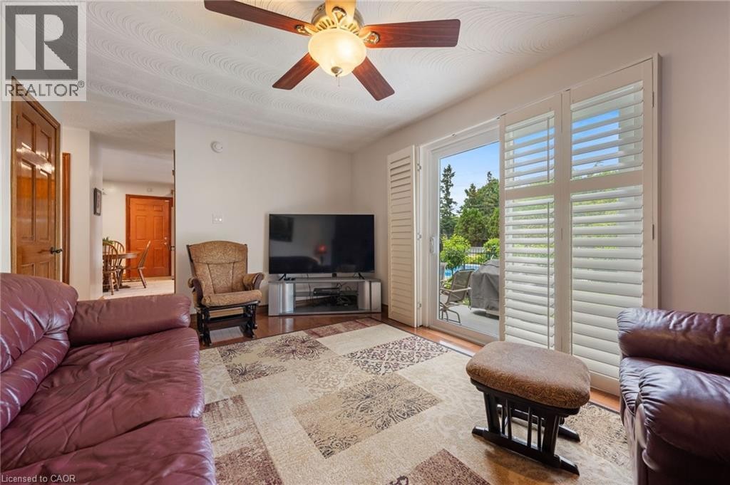 Living area featuring wood-finish flooring, a ceiling fan, and white plantation shutters on the sliding glass door - 7 Thomson Road, Simcoe, ON
