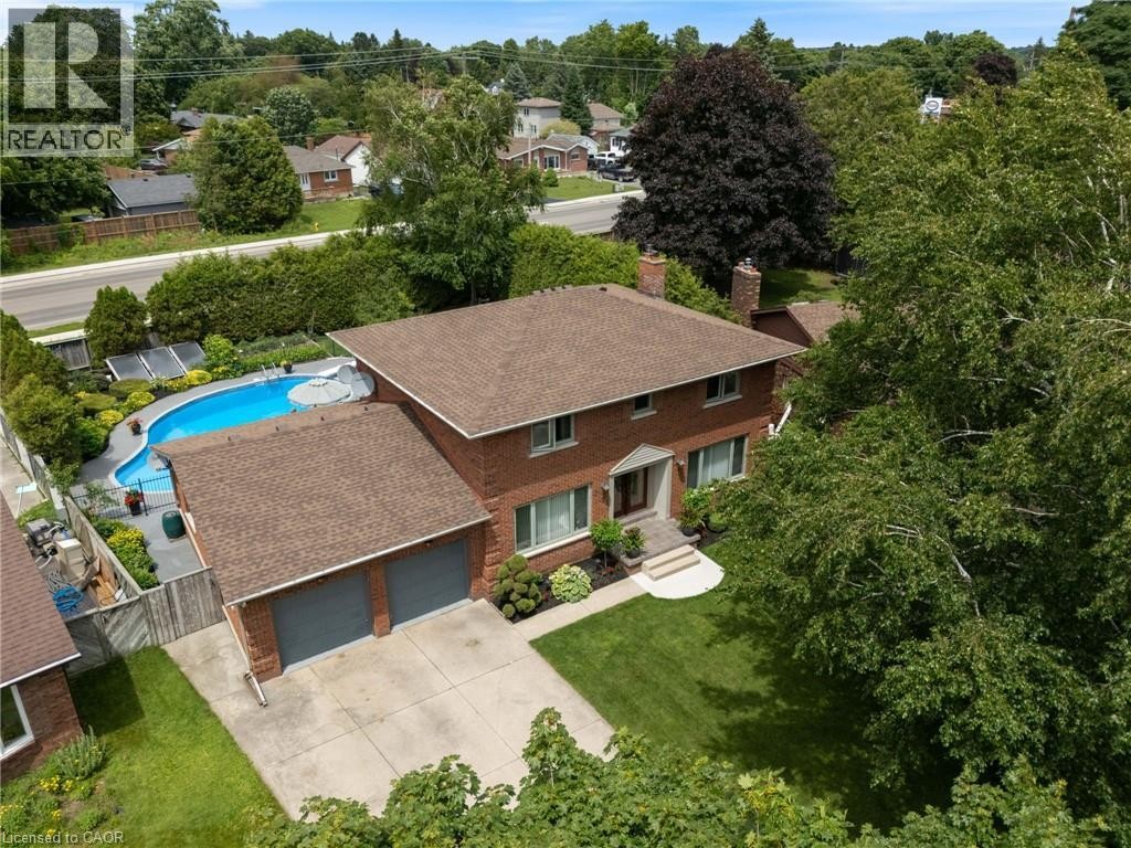 Brick exterior residence featuring a two-car garage, mature landscaping, a paved driveway, and an in-ground swimming pool - 7 Thomson Road, Simcoe, ON