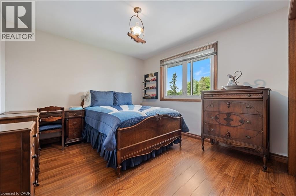 Bright bedroom featuring wood-finish flooring, a large window with natural light, a ceiling-mounted light fixture, and light-toned walls - 7 Thomson Road, Simcoe, ON