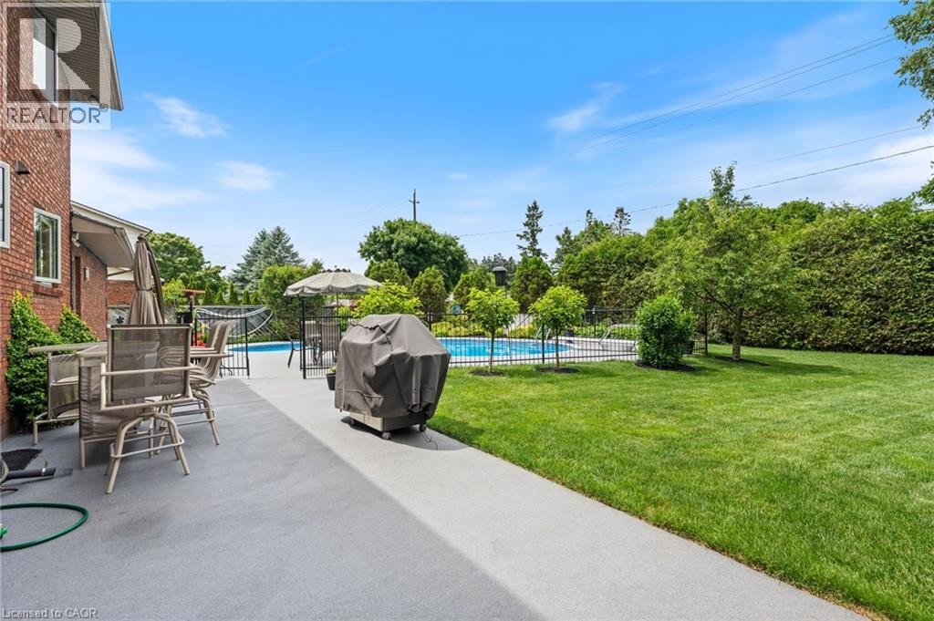 Spacious backyard featuring a large green lawn, a fenced-in swimming pool, a concrete patio area, and mature perimeter landscaping - 7 Thomson Road, Simcoe, ON
