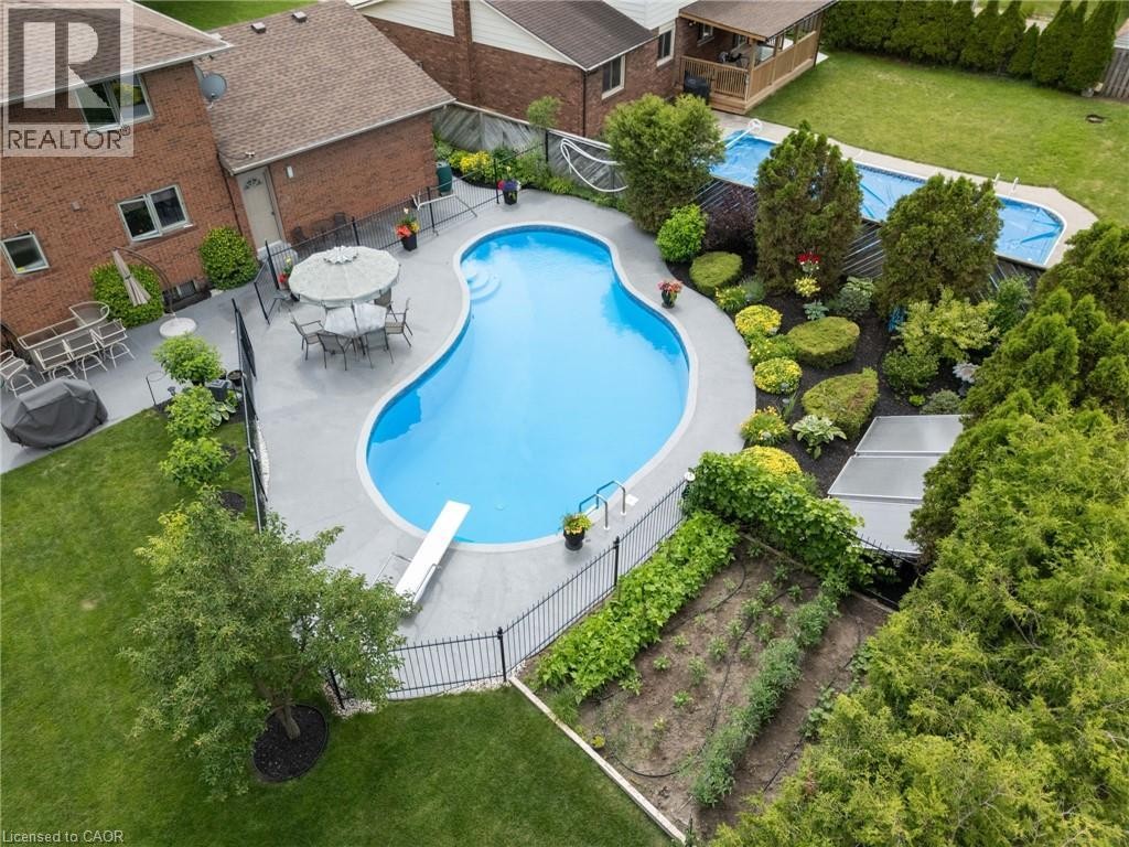 Curved swimming pool with an integrated diving board, surrounded by a gray paved patio - 7 Thomson Road, Simcoe, ON