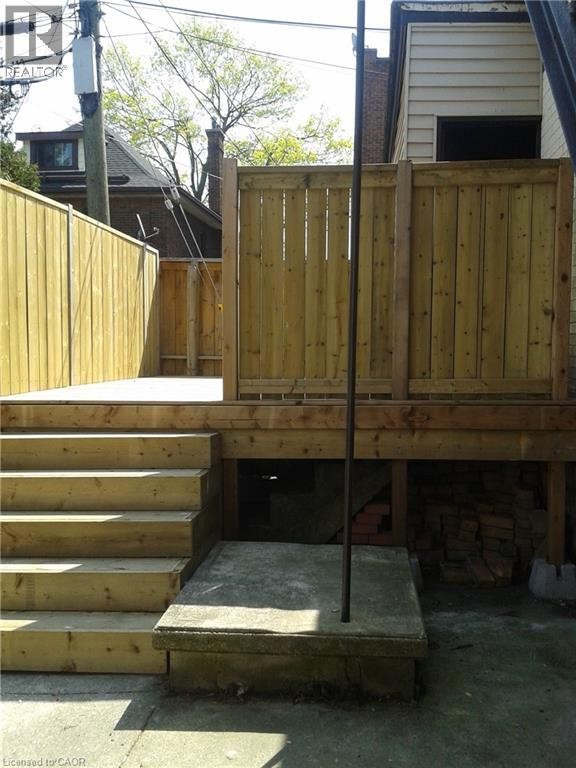 Elevated wood deck with privacy fencing, featuring a multi-step staircase and concrete patio access - 947 Main Street E, Hamilton, ON