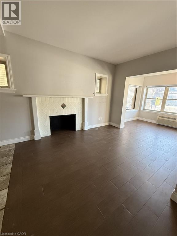 Living area featuring wood-finish flooring, a tiled fireplace surround, and multiple windows - 947 Main Street E, Hamilton, ON - Indoor Photo Showing Other Room