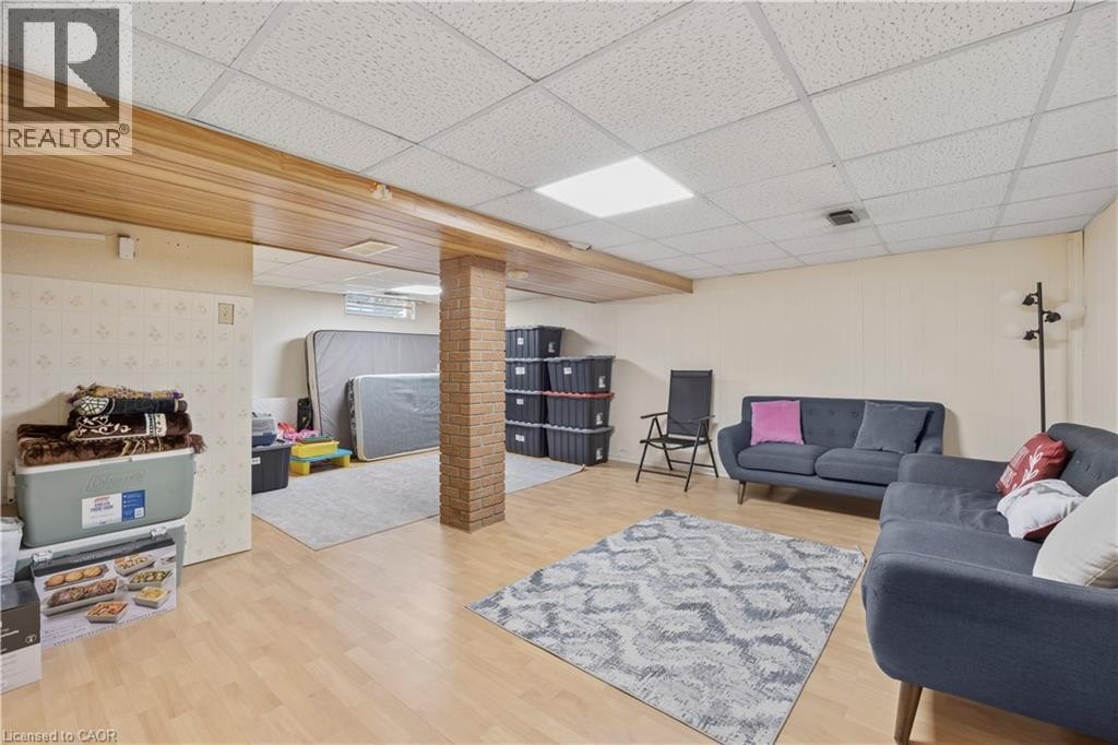 Spacious finished room featuring light wood-finish flooring, a brick-clad support column, and a drop ceiling with recessed lighting - 277 Blackacres Boulevard, London, ON