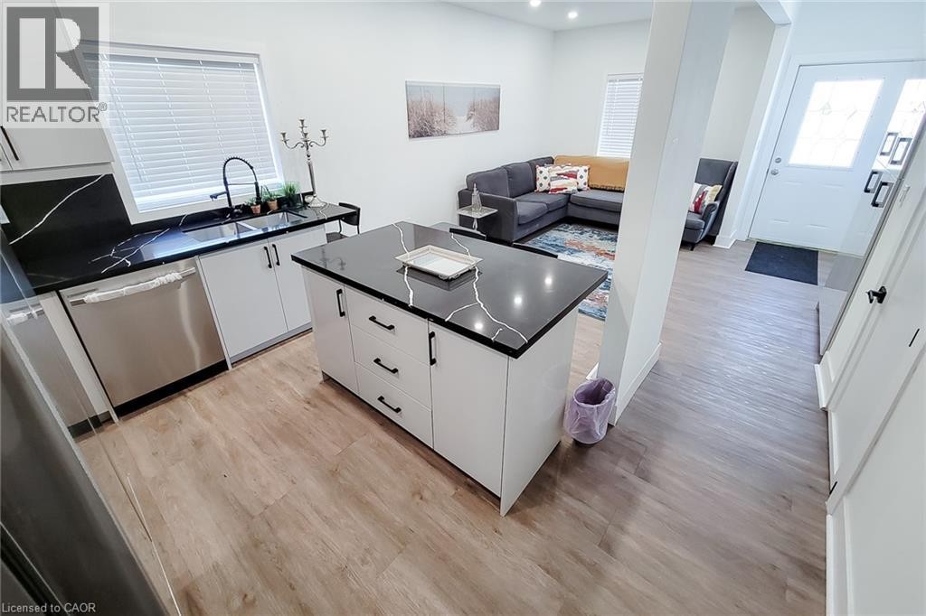 Contemporary kitchen featuring white cabinetry, black countertops with white veining, a stainless steel dishwasher, and a central island - 78 Hillyard Street, Hamilton, ON