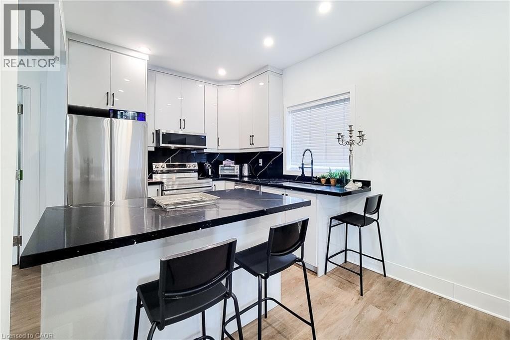 Contemporary kitchen featuring glossy white cabinetry, dark countertops, a built-in stainless steel refrigerator, and recessed lighting - 78 Hillyard Street, Hamilton, ON