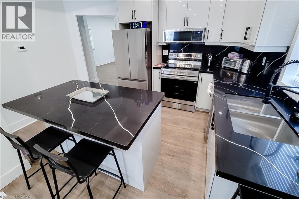 Kitchen featuring a central island with a dark countertop, light wood-finish flooring, white upper and lower cabinetry, stainless steel appliances, and a dark backsplash - 78 Hillyard Street, Hamilton, ON