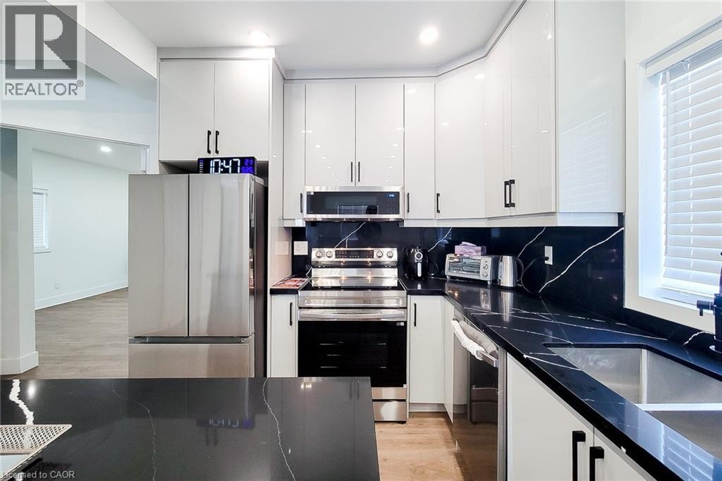Modern kitchen featuring white glossy cabinetry, dark countertops with white veining, stainless steel appliances, and a stainless steel double basin sink - 78 Hillyard Street, Hamilton, ON