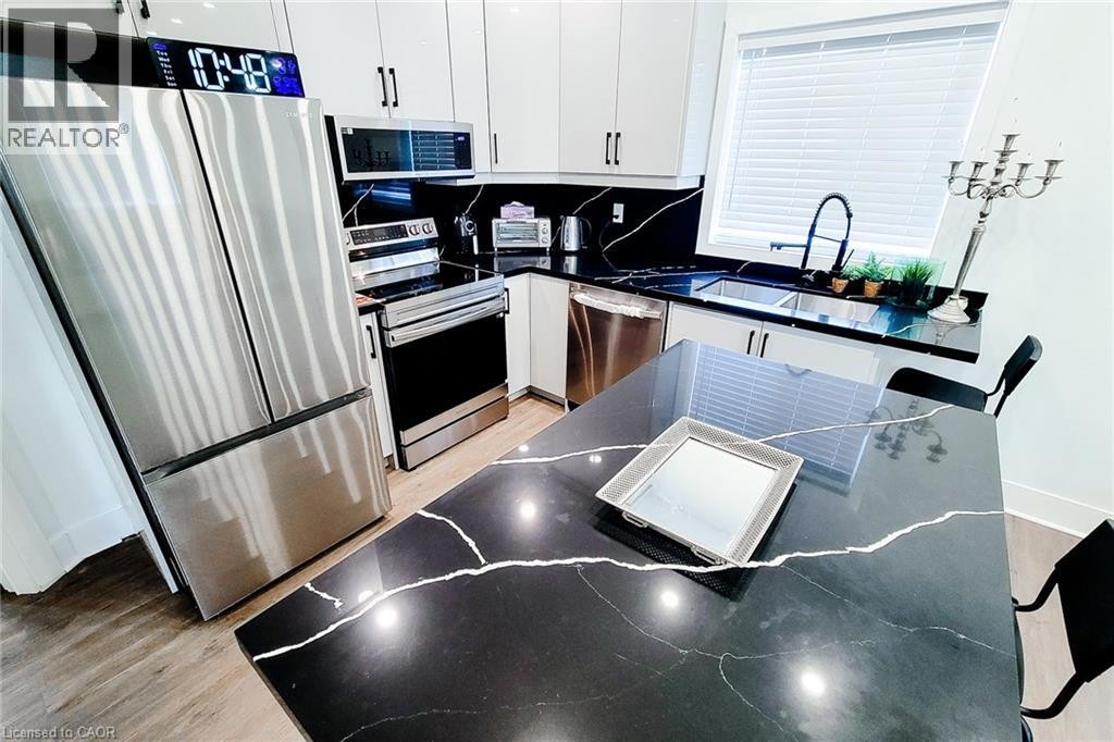 Modern kitchen featuring black countertops with white veining, white cabinetry, and stainless steel appliances - 78 Hillyard Street, Hamilton, ON