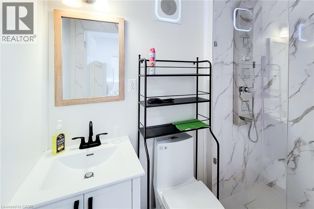 Contemporary bathroom featuring a white vanity with a black faucet, a framed mirror, a modern toilet, and a walk-in shower with marble-look wall tiling and a stainless steel shower panel - 78 Hillyard Street, Hamilton, ON