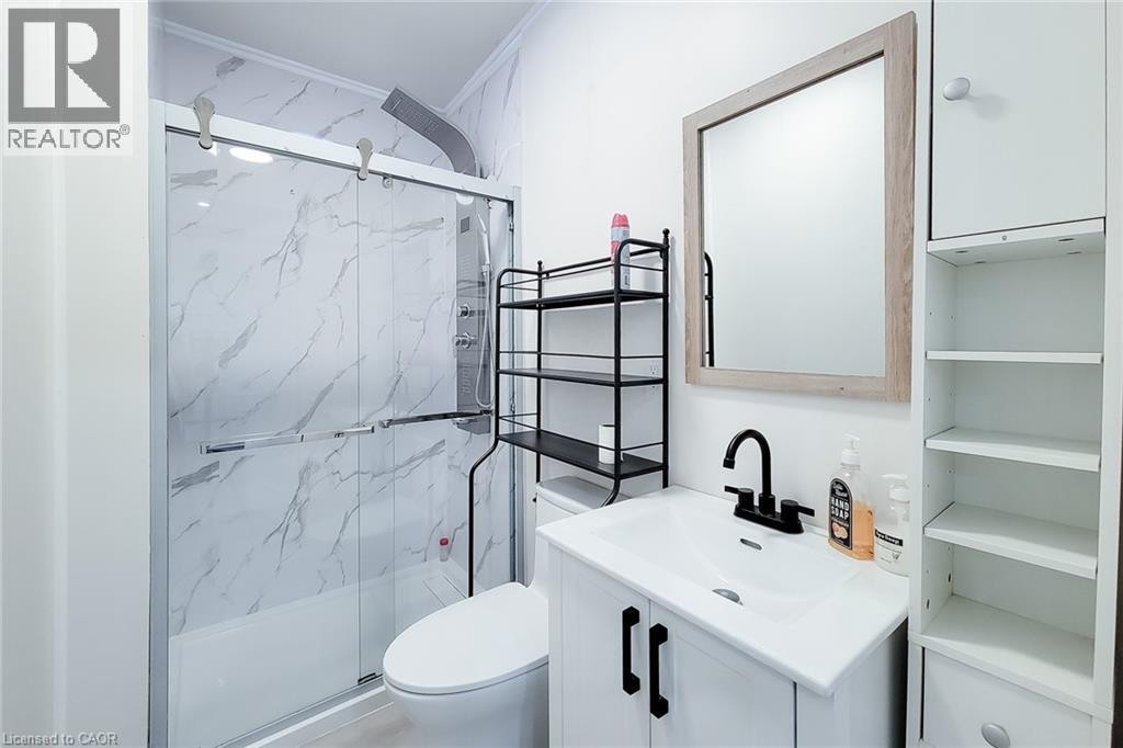 Bathroom featuring a white vanity with a black faucet, a rectangular mirror with a wood-finish frame, and white wall-mounted cabinetry with open shelving - 78 Hillyard Street, Hamilton, ON