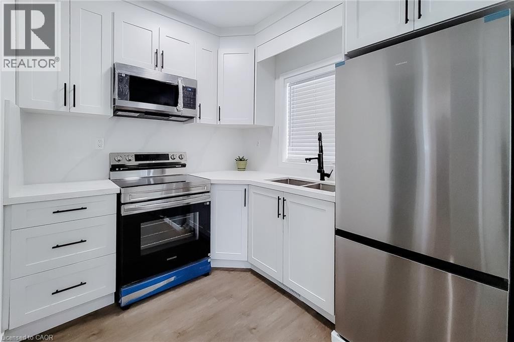 Kitchen featuring white shaker-style cabinetry, stainless steel appliances, light-toned countertops, and wood-finish flooring - 78 Hillyard Street, Hamilton, ON