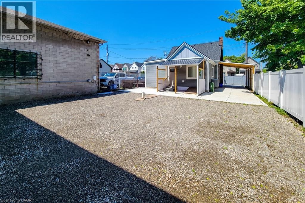 Expansive gravel area offering ample parking, featuring a white privacy fence and a concrete drive leading to a covered carport - 78 Hillyard Street, Hamilton, ON