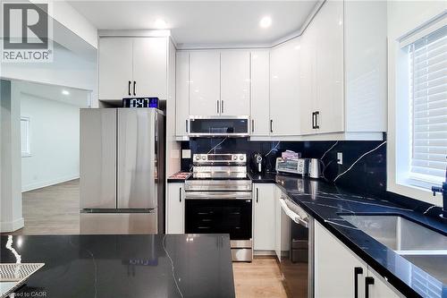 Modern kitchen featuring white glossy cabinetry, dark countertops with white veining, stainless steel appliances, and a stainless steel double basin sink - 78 Hillyard Street, Hamilton, ON 