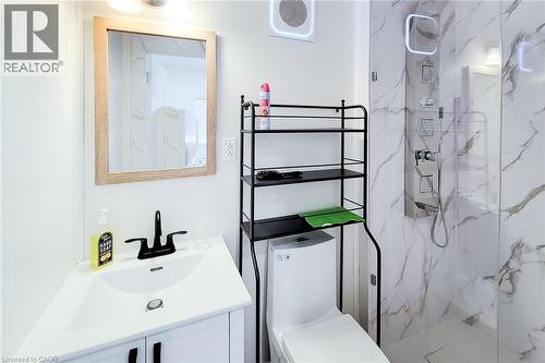 Contemporary bathroom featuring a white vanity with a black faucet, a framed mirror, a modern toilet, and a walk-in shower with marble-look wall tiling and a stainless steel shower panel - 78 Hillyard Street, Hamilton, ON 