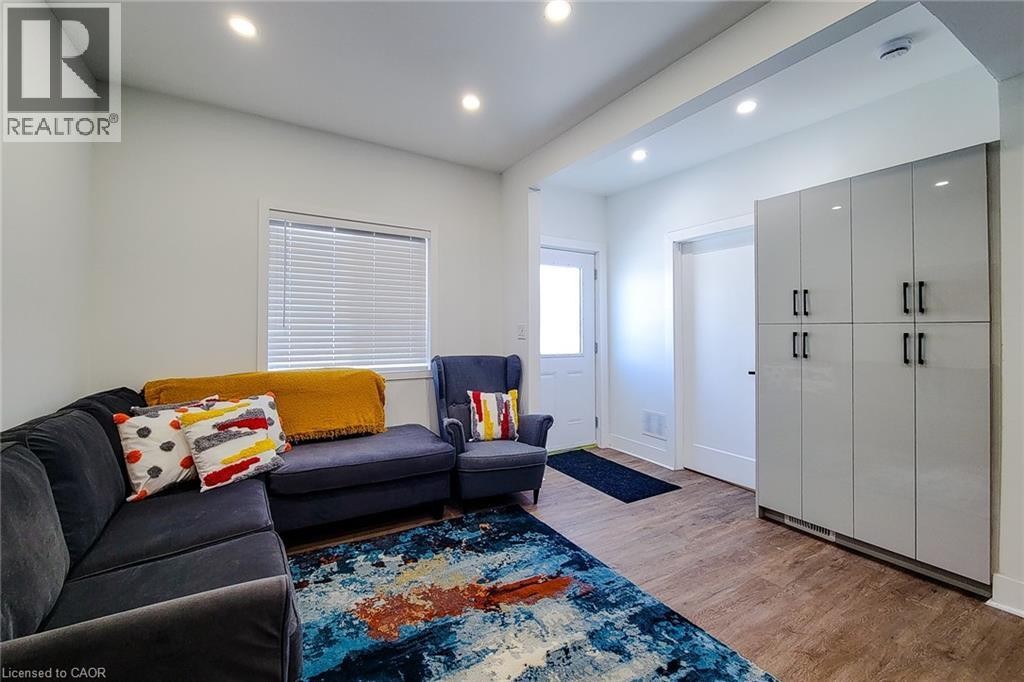 Spacious living area featuring wood-finish flooring, recessed lighting, a white framed window with blinds, and built-in glossy light gray cabinetry with black hardware - 78 Hillyard Street, Hamilton, ON