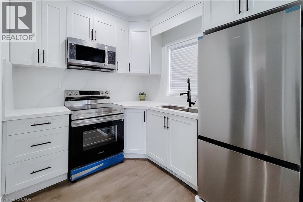 Kitchen featuring white shaker-style cabinetry, stainless steel appliances, light-toned countertops, and wood-finish flooring - 78 Hillyard Street, Hamilton, ON