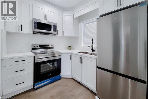 Kitchen featuring white shaker-style cabinetry, stainless steel appliances, light-toned countertops, and wood-finish flooring - 78 Hillyard Street, Hamilton, ON 