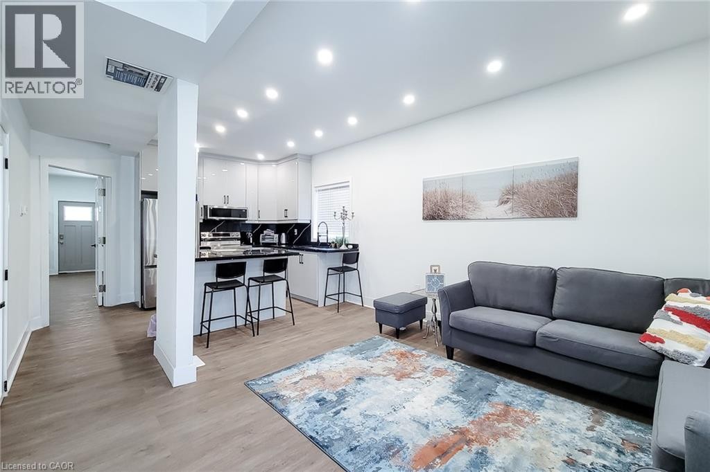 Open-concept living space featuring wood-finish flooring, recessed lighting, and a kitchen with white gloss cabinetry and dark countertops - 78 Hillyard Street, Hamilton, ON