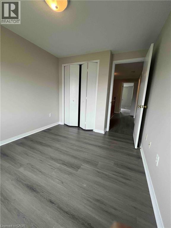 Interior room featuring wood-finish flooring, light neutral wall paint, white baseboards, and a bi-fold closet door - 151 Clairfields Drive E Unit# 4, Guelph, ON