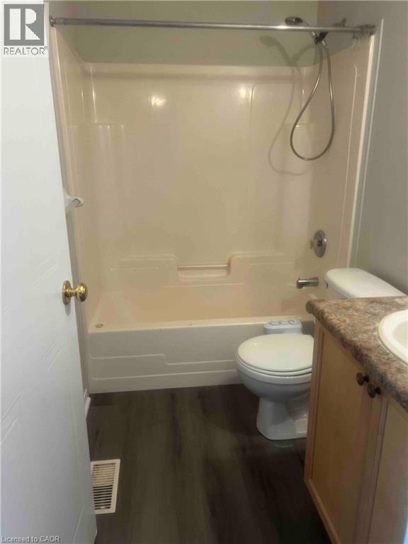 Bathroom featuring a white tub/shower combination, dark wood-finish flooring, a toilet, a light wood vanity with a light-colored countertop, and a white sink - 151 Clairfields Drive E Unit# 4, Guelph, ON