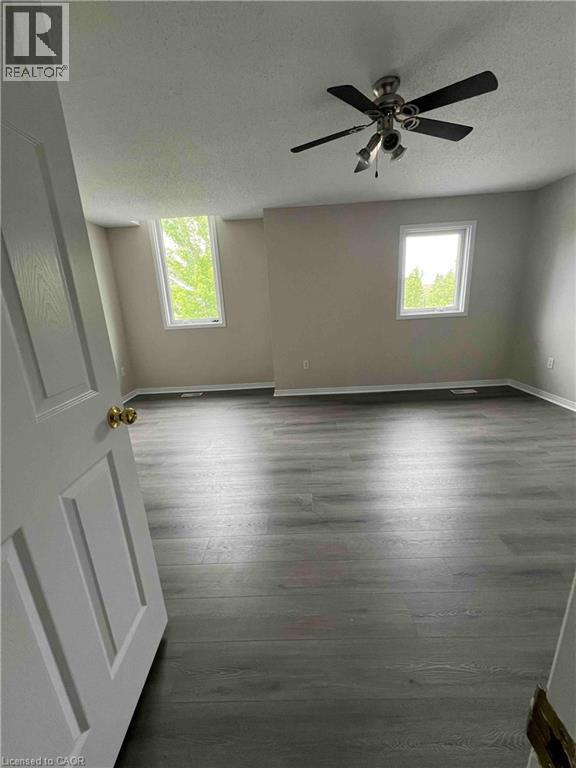Spacious room featuring wood-finish flooring, two windows, and a ceiling fan with integrated lighting - 151 Clairfields Drive E Unit# 4, Guelph, ON
