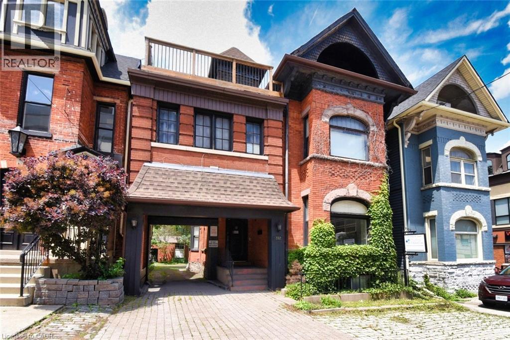 Brick facade building featuring a covered entryway, paved driveway, and stone retaining wall - 242 James Street S, Hamilton, ON