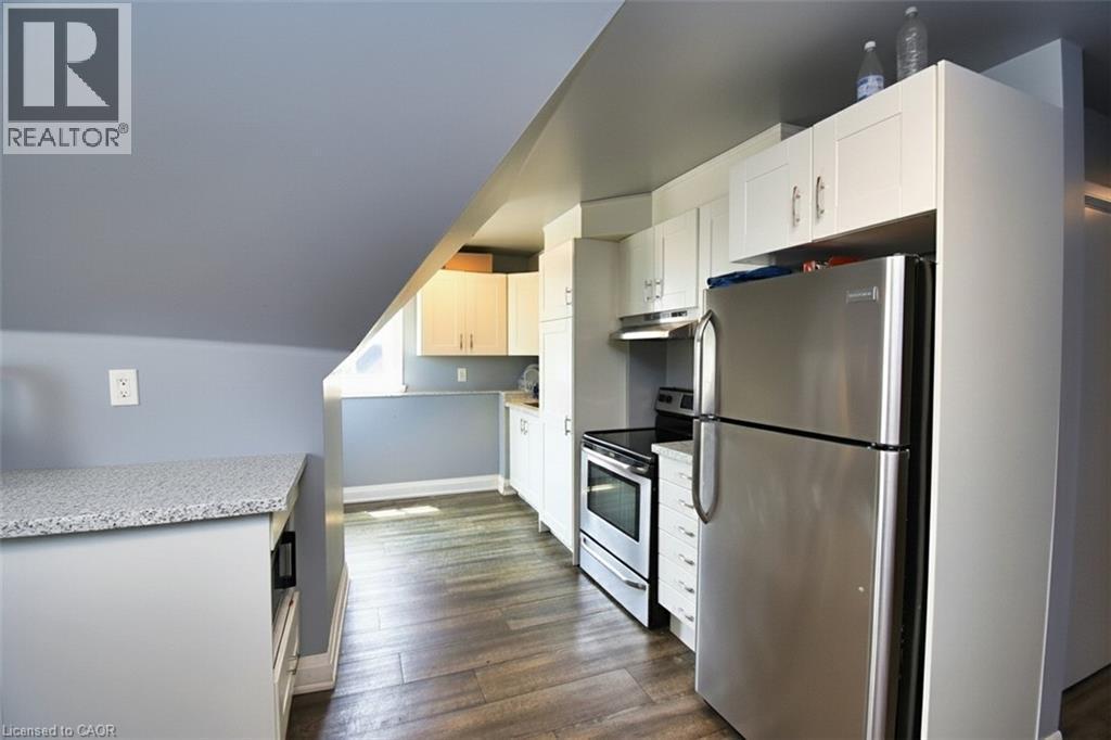 Kitchen featuring stainless steel appliances, white cabinetry, wood-finish flooring, light-toned countertops, and a built-in electric range with exhaust hood - 242 James Street S, Hamilton, ON