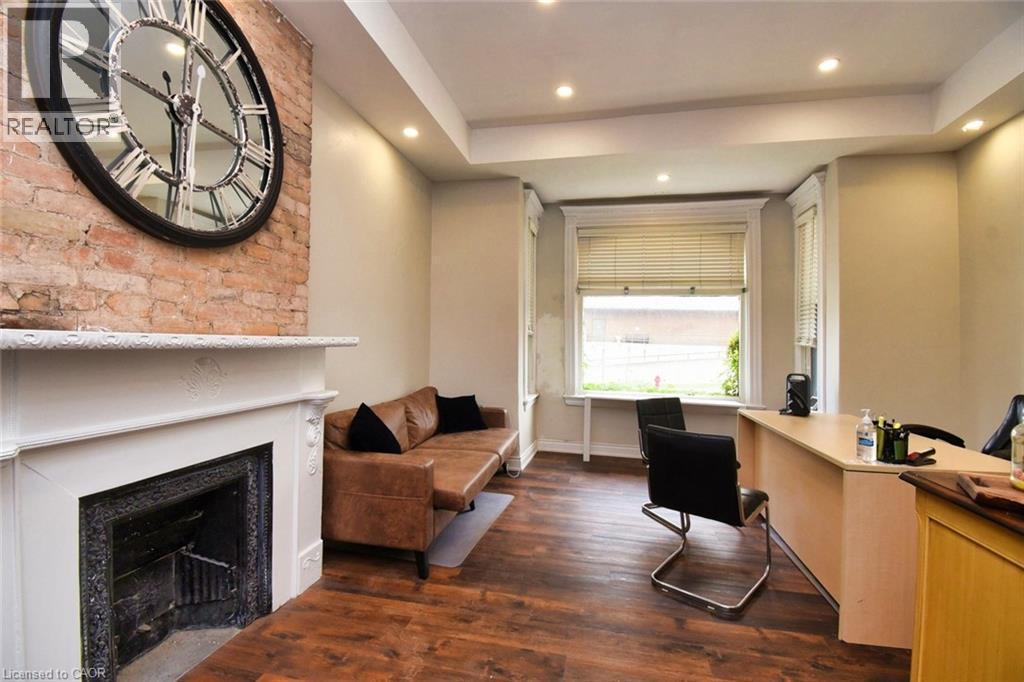 Exposed brick accent wall featuring a decorative fireplace with a white mantel, wood-finish flooring, recessed lighting, and bay windows - 242 James Street S, Hamilton, ON
