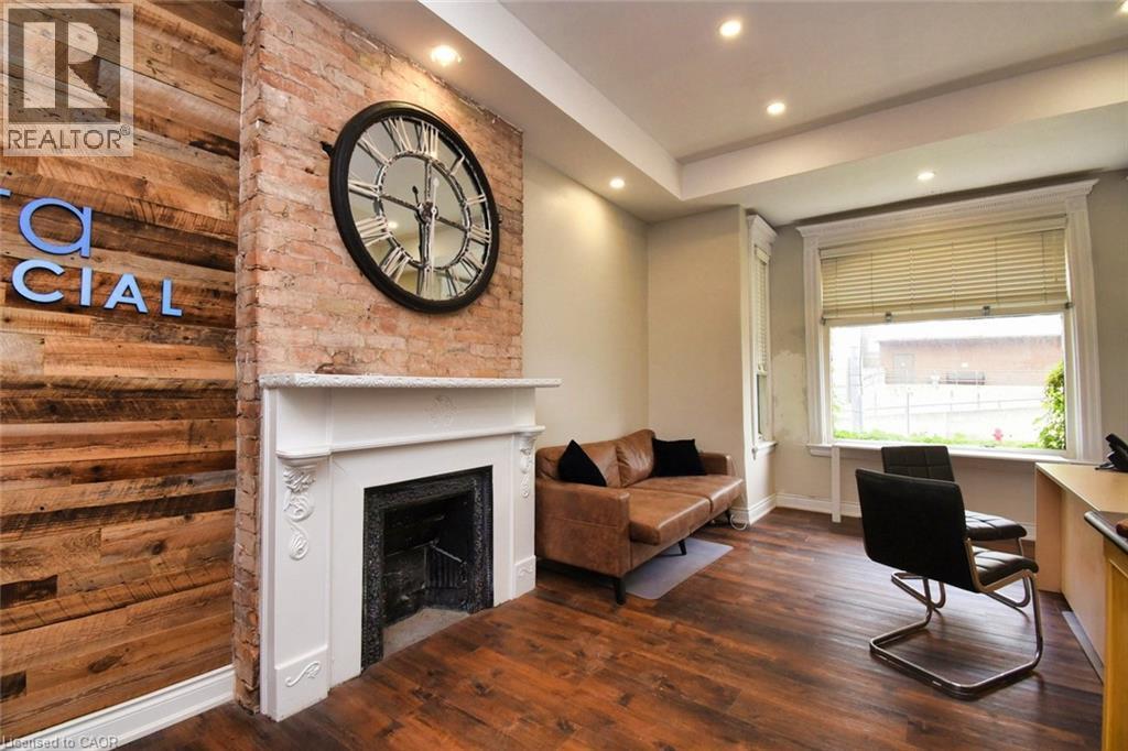 Exposed brick wall featuring a decorative fireplace with a white mantel, complemented by wood-finish flooring and recessed lighting - 242 James Street S, Hamilton, ON