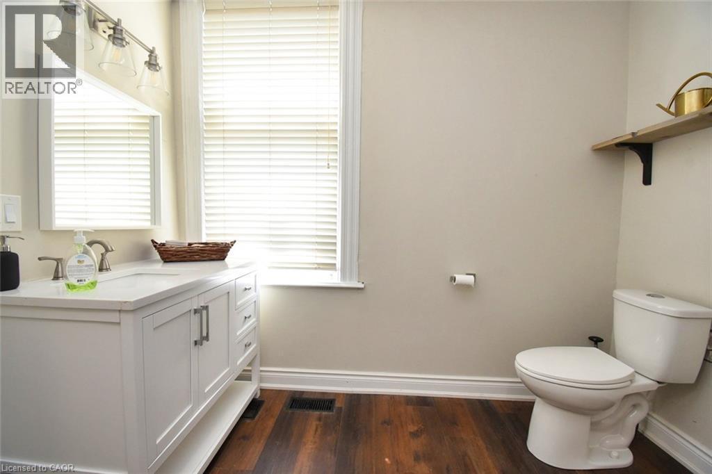 Bathroom featuring a white vanity with integrated sink, brushed nickel faucet, and a large mirror with a three-light fixture - 242 James Street S, Hamilton, ON