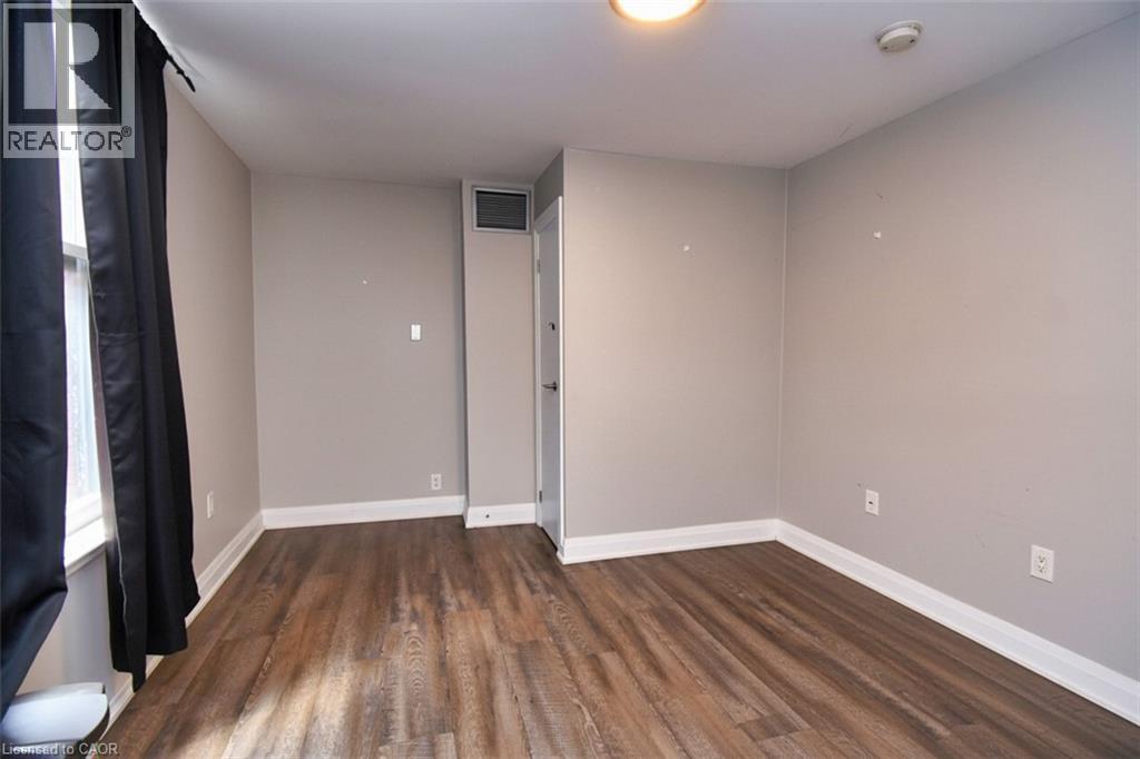 Room featuring wood-finish flooring, light grey walls, white baseboards, and a flush-mount ceiling light fixture - 242 James Street S, Hamilton, ON