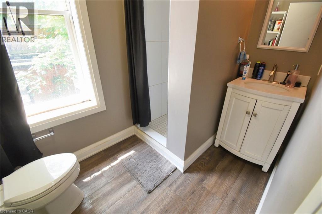 Bathroom featuring wood-finish flooring, a white vanity with integrated sink, and a white toilet - 242 James Street S, Hamilton, ON