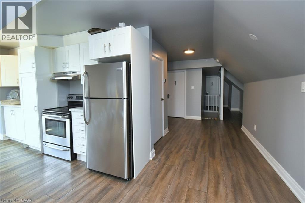 Kitchenette featuring a stainless steel refrigerator and range, white cabinetry, light countertops, and wood-finish flooring - 242 James Street S, Hamilton, ON