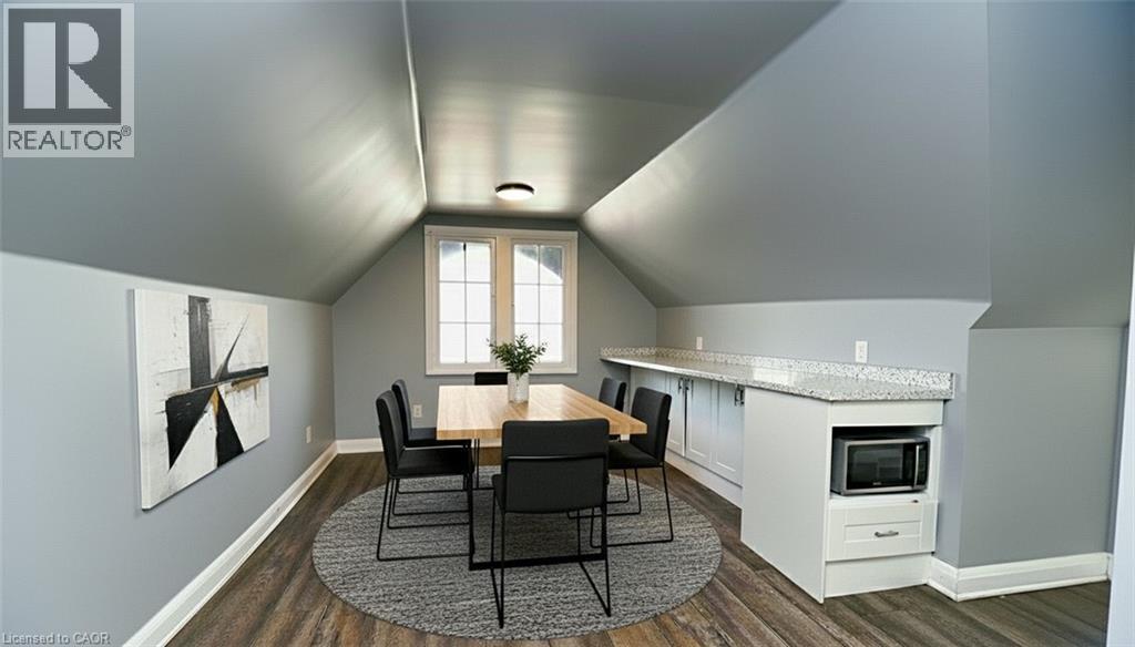 Attic space featuring wood-finish flooring, a contemporary ceiling light fixture, white baseboards, and a built-in countertop with white cabinetry - 242 James Street S, Hamilton, ON
