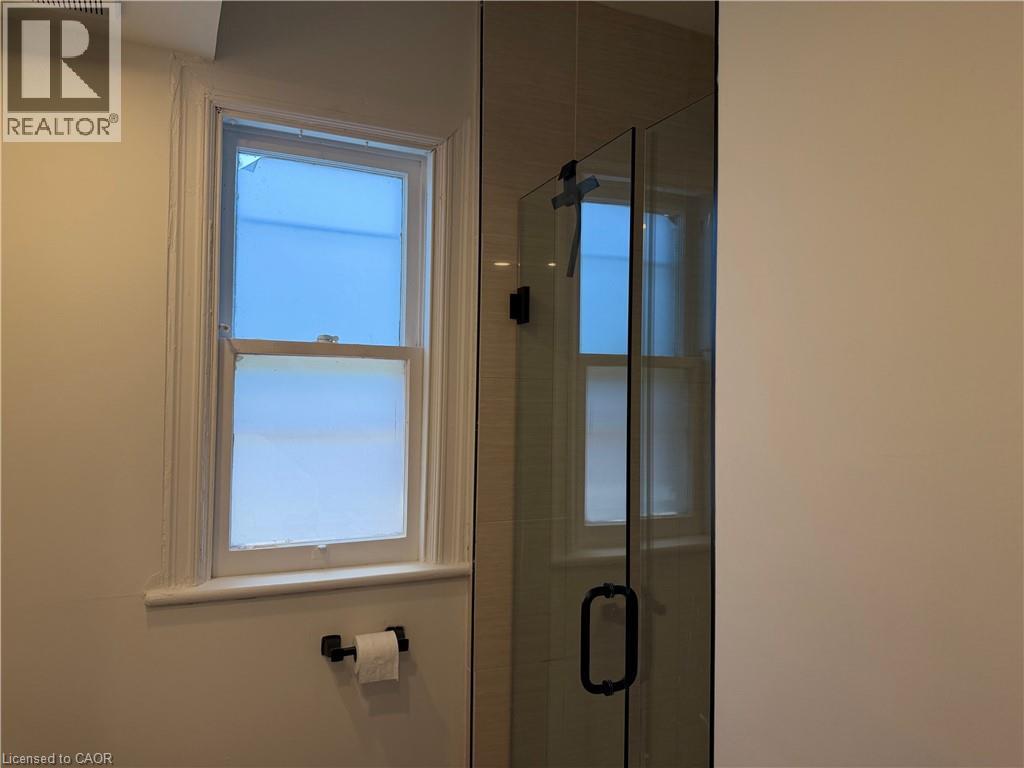 Frosted window with white trim, matte black toilet paper holder, and a clear glass shower enclosure with matte black hardware - 207 Charlton Avenue W, Hamilton, ON