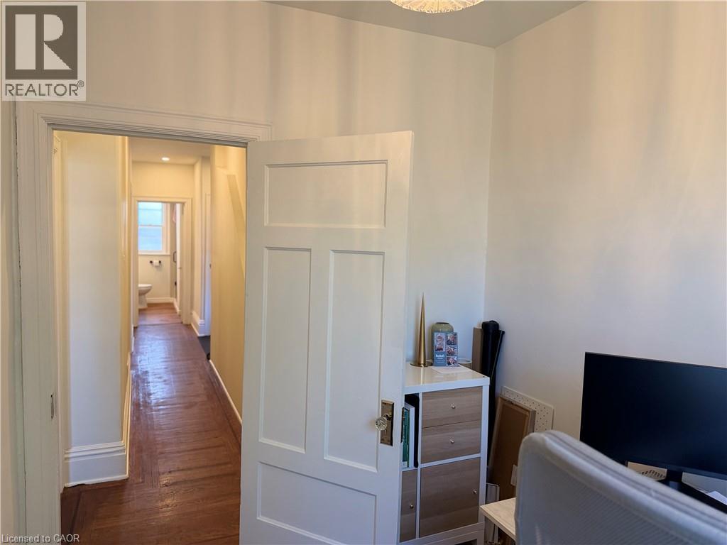 Hallway with wood-finish flooring, white trim, and recessed lighting leading to a bathroom with a window - 207 Charlton Avenue W, Hamilton, ON