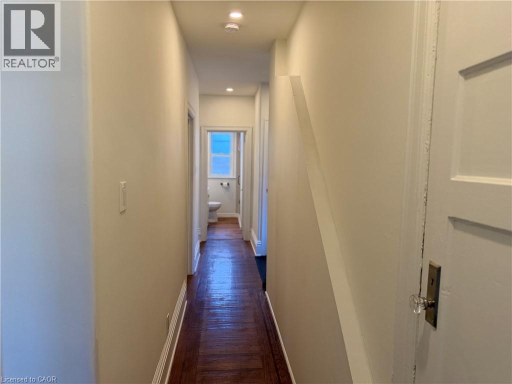 Hallway featuring wood-finish flooring, recessed lighting, and a white interior door with a clear glass knob - 207 Charlton Avenue W, Hamilton, ON