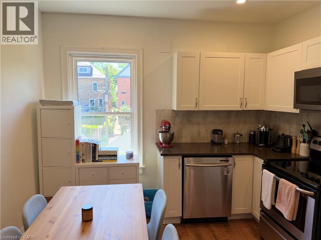 Kitchen featuring white shaker-style cabinetry, a dark countertop, and a tiled backsplash - 207 Charlton Avenue W, Hamilton, ON