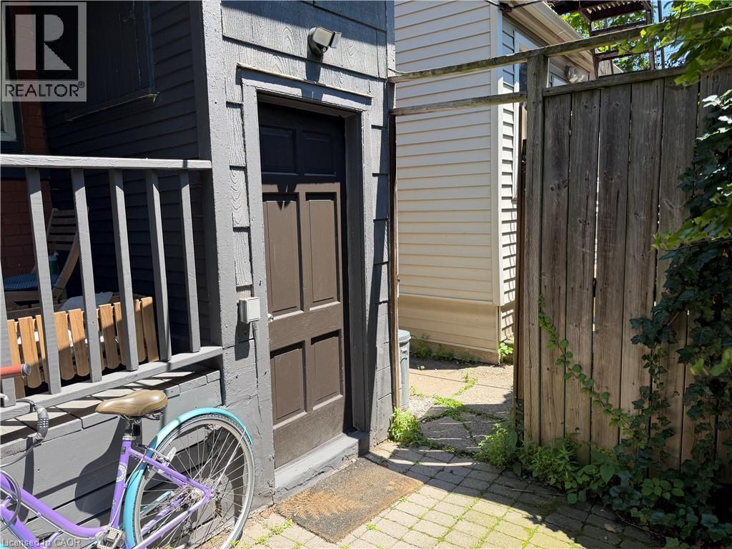 Exterior entrance with dark brown paneled door, gray wood siding, and an overhead light fixture - 207 Charlton Avenue W, Hamilton, ON
