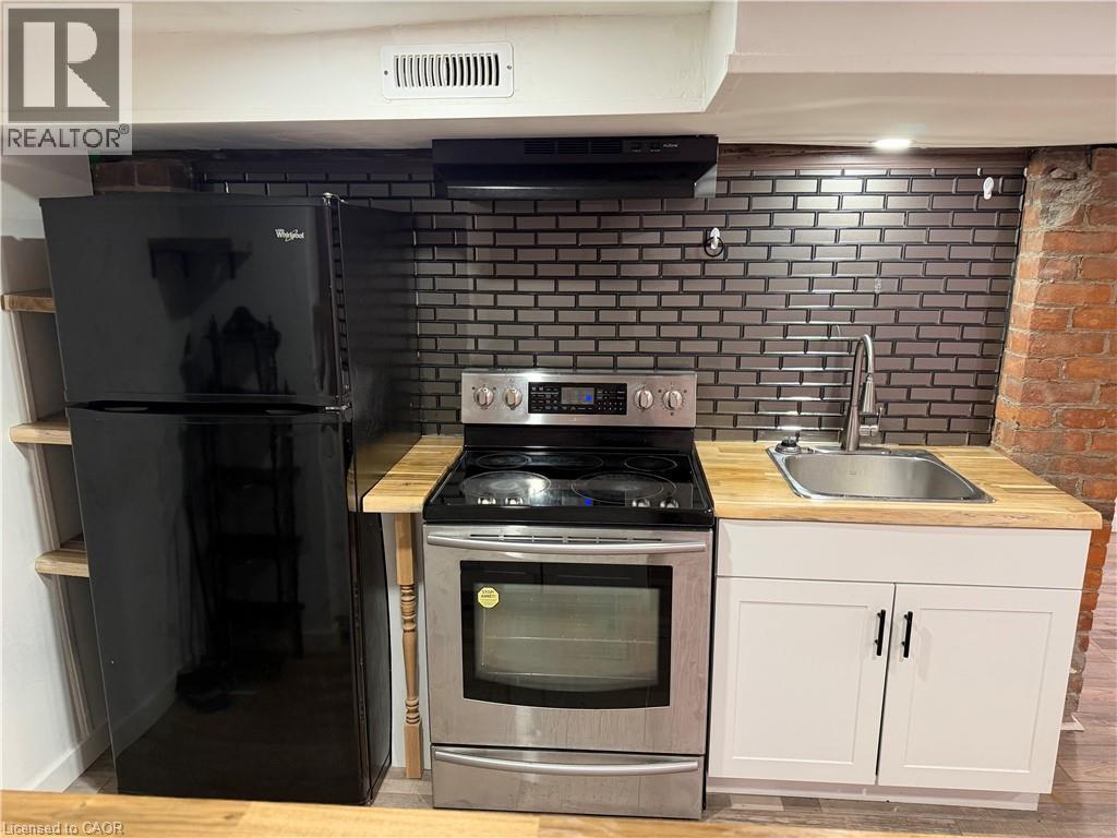 Compact kitchen area featuring a stainless steel electric range, black refrigerator, stainless steel sink with a high-arch faucet, and wood-finish countertops - 207 Charlton Avenue W, Hamilton, ON