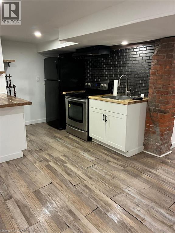 Wood-finish flooring, white cabinetry, stainless steel range, black refrigerator, and a black subway tile backsplash - 207 Charlton Avenue W, Hamilton, ON