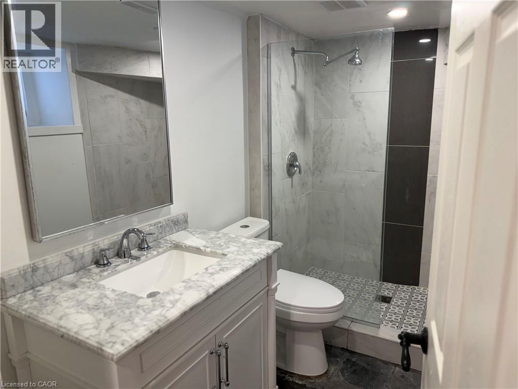 Bathroom featuring a white vanity with a marble-finish countertop, undermount sink, and chrome fixtures - 207 Charlton Avenue W, Hamilton, ON