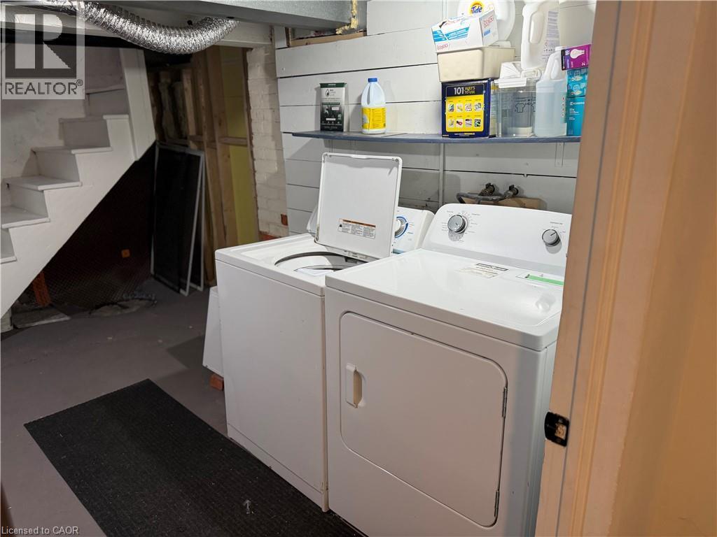Laundry area featuring a top-load washing machine, front-load dryer, wall-mounted shelving, and concrete flooring - 207 Charlton Avenue W, Hamilton, ON