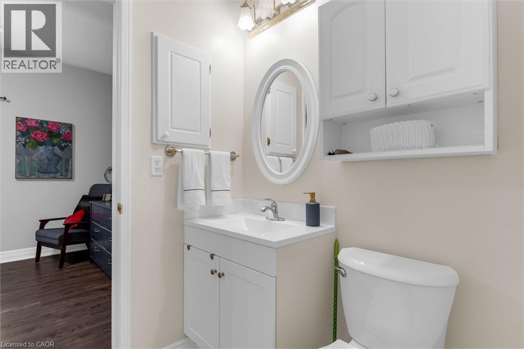 Powder room featuring a white vanity with integrated sink, an oval mirror, and a wall-mounted cabinet with open shelving - 149 Silverbirch Boulevard, Hamilton, ON