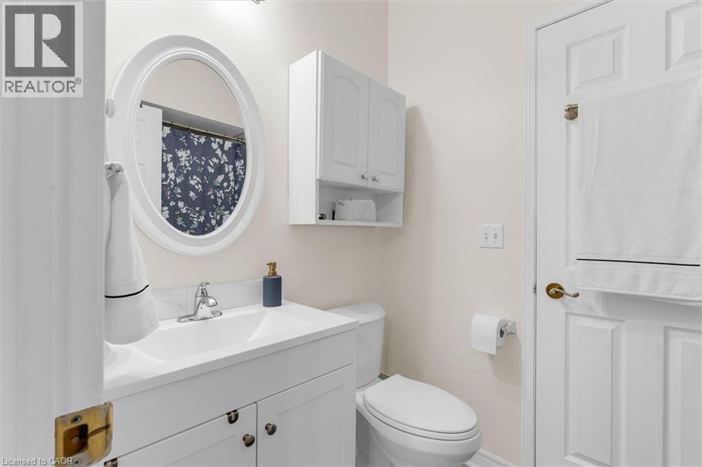 Bathroom featuring a white vanity with an integrated sink, polished chrome faucet, an oval mirror, and a wall-mounted storage cabinet - 149 Silverbirch Boulevard, Hamilton, ON
