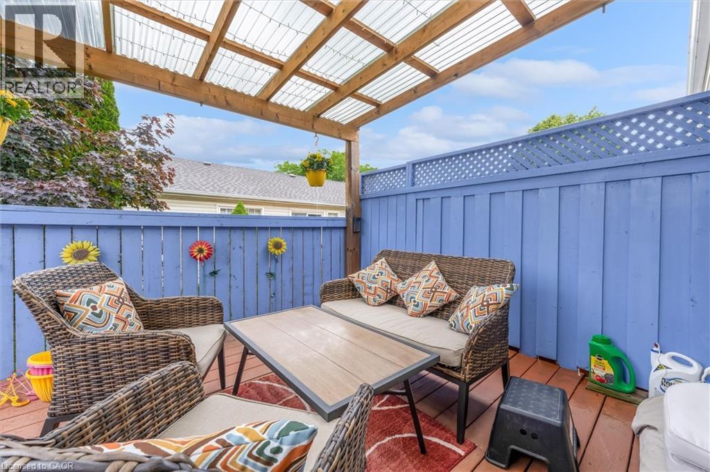 Outdoor patio featuring a wood-finish deck, a blue privacy fence with lattice top, and a translucent corrugated roof supported by a wood frame - 149 Silverbirch Boulevard, Hamilton, ON