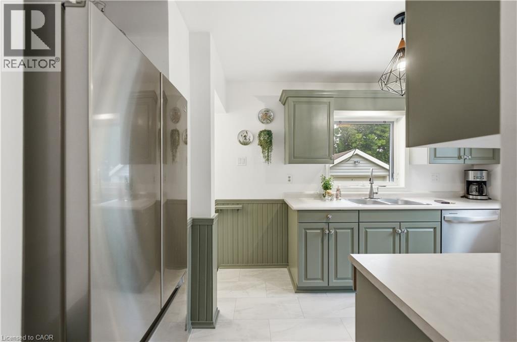 Kitchen featuring stainless steel appliances, sage green cabinetry, a double basin sink with a chrome faucet, light-toned countertops, and beadboard wainscoting - 81 Vale Avenue, St. Catharines, ON