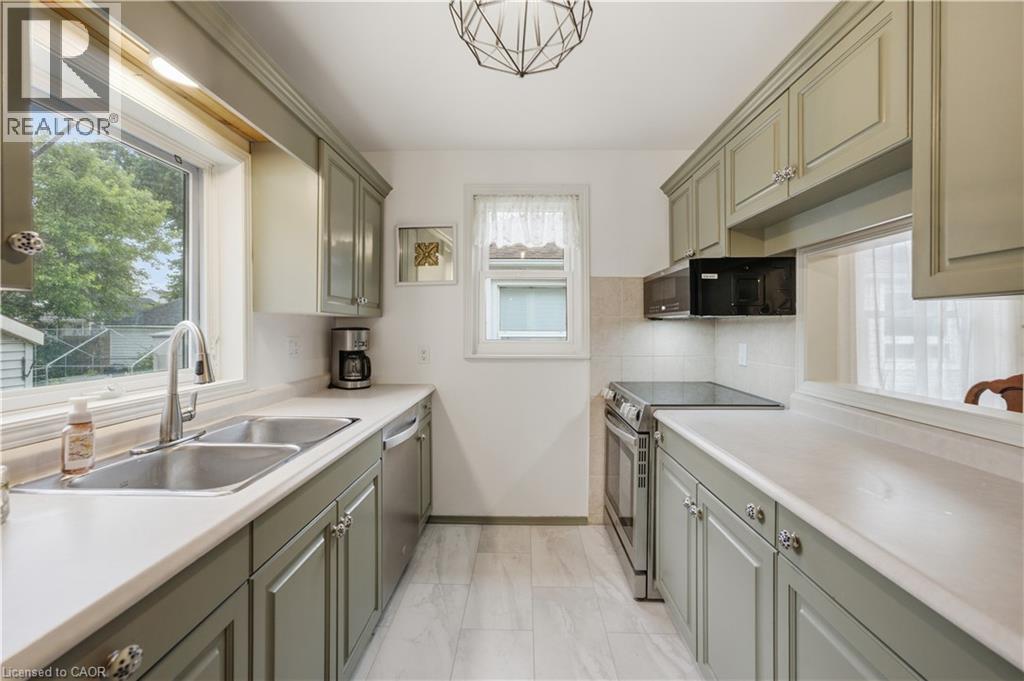 Galley kitchen featuring light green cabinetry, white countertops, tile backsplash, and stainless steel appliances - 81 Vale Avenue, St. Catharines, ON