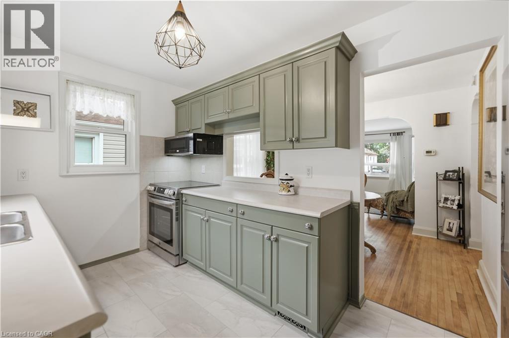 Kitchen featuring painted cabinetry, light countertops, stainless steel appliances, and a geometric pendant light fixture - 81 Vale Avenue, St. Catharines, ON